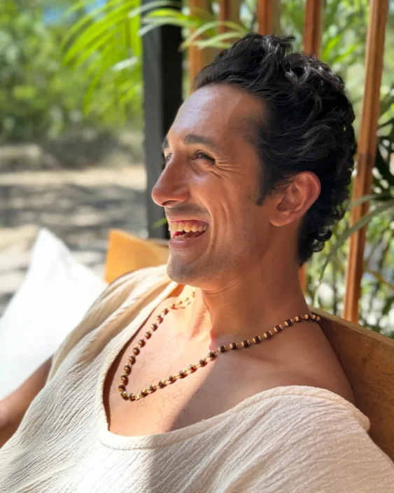 Raj laughing in the sun, seated on a wooden porch among palms